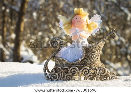 A toy angel sits in a golden sleigh on the snow. Christmas toys