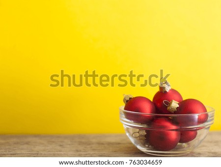 Some Red balls in plate on light wooden table and yellow wall background. Christmas Tree. New Year Time.