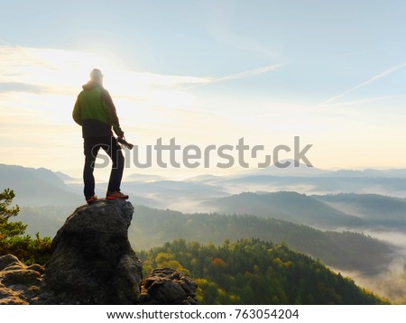 Photographer looks into the landscape and listen the silence. Man prepare camera to takes impressive photos of  misty fall mountains.