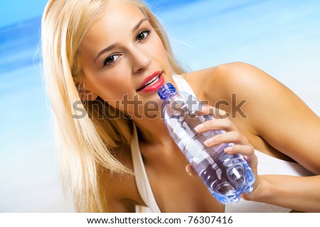Portrait of young woman drinking water on beach