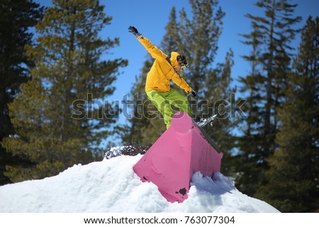 Young men jib on a snowboard in terrain park wearing yellow jacket and green pants. It is snow time during winter in a mountain ski resort in California. Royalty-Free Stock Photo #763077304
