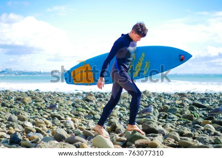 Male surfer carry blue short surf board. Young man wearing wetsuit walking to the ocean. Topanga stone beach, California, USA. American surfer.  Royalty-Free Stock Photo #763077310