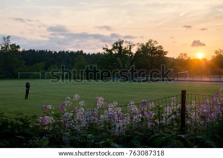 A young woman stands in a soccer field and takes a picture of a sunset. Photographed in Groton, MA in May 2012. 