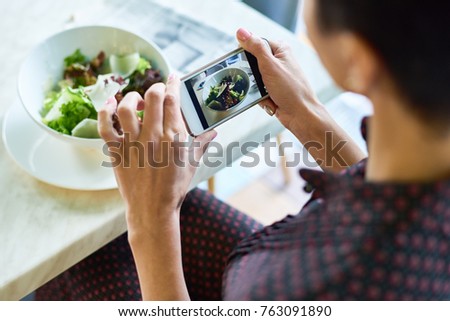 Close up of unrecognizable woman taking photos of food in cafe, focus on salad bowl in smartphone screen