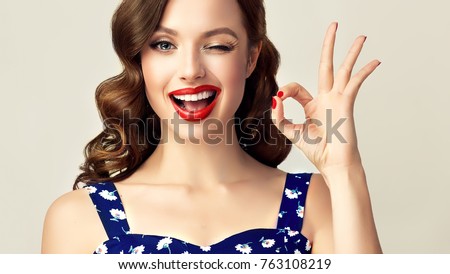 Pin-up retro girl with curly hair  winking, smiling and showing OK sign . Presenting your product. Expressive facial expressions