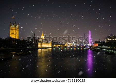 Night time view across river Thames a cold winter night with falling snow, London, United Kingdom