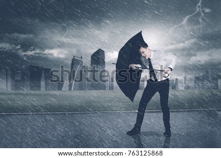 Picture of American businessman using an umbrella while protecting himself from storm