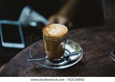 Coffee cup on the wooden board with blurred smartphone and camera, vintage tone