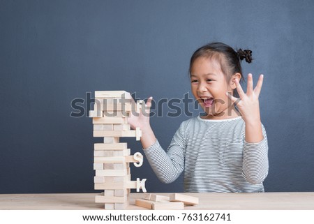 Portrait of kid cute asian girl age 6 year happy to play blocks wood game with word risk on tower wood block wooden table background. With copy space for text .