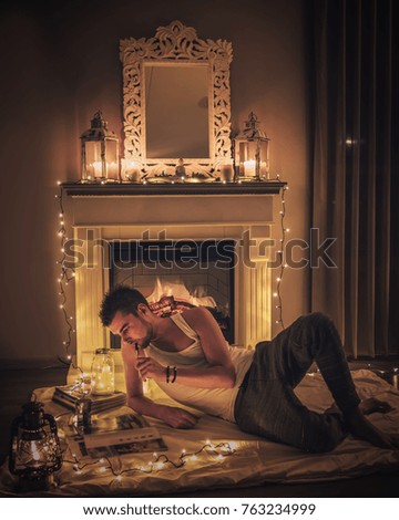 young man by a Cozy fireplace with candles blanket and books, Christmas winter home with lights