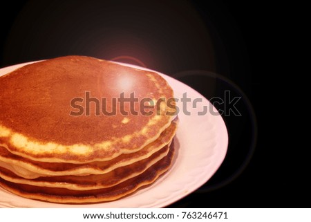 Part of the picture of a pile of pancakes with maple syrup on a white plate on a black background with a glare of light