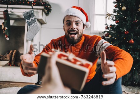 Another cute picture of a guy getting a gift from his close friend this after Christmas morning. Young man is amazed and hapy to get a present and taking it with pleasure. Close up. Cut view