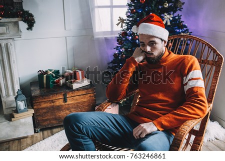 Another close up of unhappy and sad man sitting in the brown rocking chair and thinking about something. He is prepared for Christmas party but the man doesn' have a good mood at all. He hopes it will