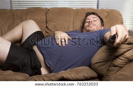 overweight man just watching tv on the couch Royalty-Free Stock Photo #763252033
