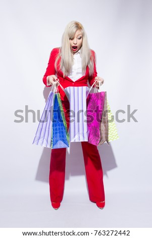 Image of young blonde lady in red costume posing with shopping bags and looking to camera over white background