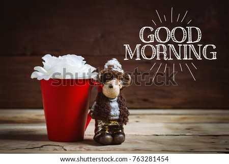 White rose flower in a red cup and toy on a wooden background. Inscription Good morning.