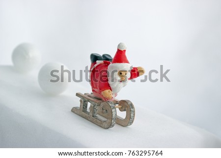 Santa Claus on the sledge descends downhill in the snow. Two big snow balls roll behind him.