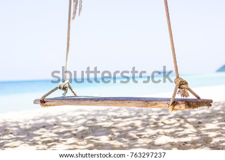 Wooden Swing on the beach Tied to a tree The background is a blur of blue and green sea of trees on the island.