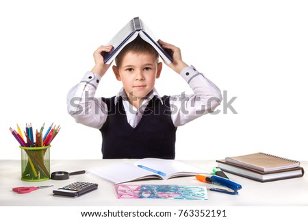Smart serious excellent pupil at the desk with open book on the head on the white background