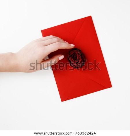 Minimalist fashion and beauty photo. A love letter in a red envelope with a rose. Female hands holding a love letter. The concept of St. Valentine's Day. Romantic photography. 14 february