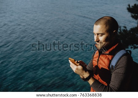 Man traveler in a red waistcoat watching world map on mobile phone while relaxing near sea 
