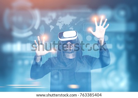 Man in VR glasses interaciting with futuristic HUD and graphs hologram against a blue background. Toned image double exposure mock up Elements of this image furnished by NASA