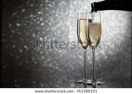 Photo of bottle with pouring champagne in wine glasses on gray background