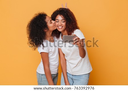 Portrait of a two happy afro american sisters taking a selfie together isolated over orange background