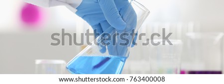 A male chemist holds test tube of glass in his hand overflows a liquid solution of potassium permanganate conducts an analysis reaction takes various versions of reagents using chemical manufacturing. Royalty-Free Stock Photo #763400008