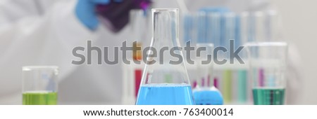 A male chemist holds test tube of glass in his hand overflows a liquid solution of potassium permanganate conducts an analysis reaction takes various versions of reagents using chemical manufacturing. Royalty-Free Stock Photo #763400014