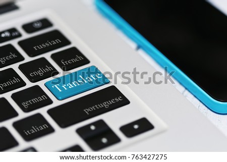 Laptop keyboard with foreign languages names including russian, greek and portuguese - online translation service metaphor. Cell phone lies nearby on wooden background. Selective focus.