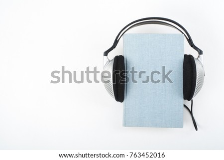Audiobook on white background. Headphones put over blue hardback book, empty cover, copy space for ad text. Distance education, e-learning concept
