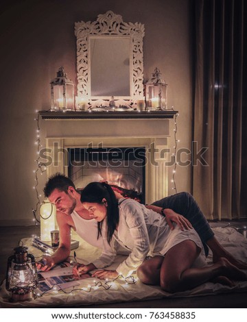 young couple man and woman by a Cozy fireplace with candles blanket and books, Christmas winter home with lights