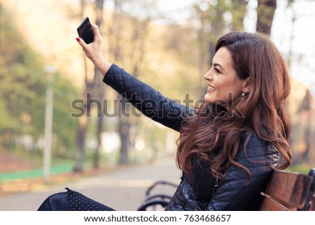 Stylish modern girl taking a selfie with smart phone in autumn park