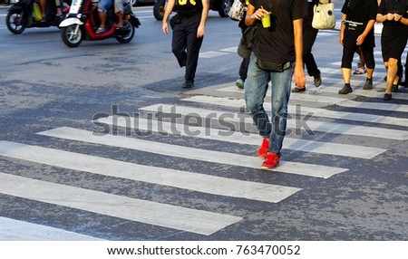 Man wearing blue jeans and red shoes holding glass of green tea crossing the street crosswalk with crowd of people during rush hour, Bangkok Thailand.