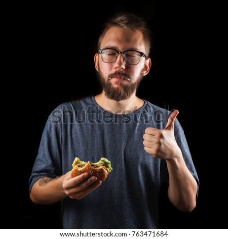 young man eating a fast food hamburger isolated on black.