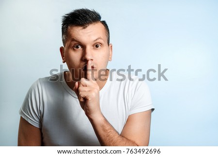 Portrait of a man close-up. Shows a hand gesture quietly, do not make noise, gesture a finger to the lips. On a light background. The concept of body language, human emotions, reaction.