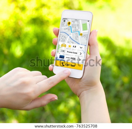 female hands holding white phone with app call taxi on screen background of green grass