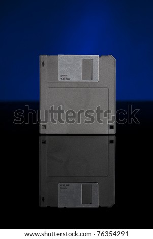 Vertical image of an obsolete floppy disk on a black reflective surface with a blue background.