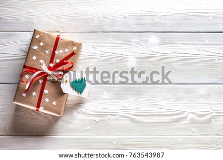Christmas present, wrapped in paper and tied with a red ribbon on a white background with snowflakes