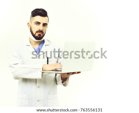Man with concentrated face in white coat. Doctor with beard type on his white laptop. Treatment and medical technologies concept. Physician in surgical mask isolated on white background, copy space