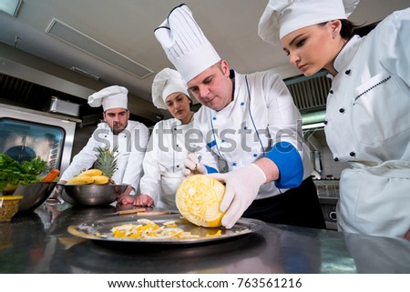 Kitchen chef with young apprentices, teaching to make decorative fruit basket Royalty-Free Stock Photo #763561216