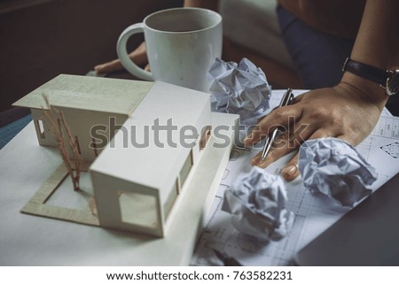 Closeup image of a stressed architects thinking and drawing shop drawing paper with architecture model and laptop on table while fail