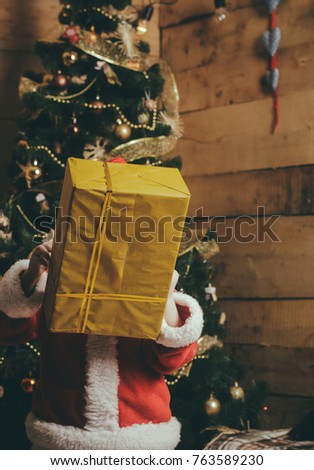 Santa claus kid at Christmas tree. Xmas party celebration. New year baby, boxing day. Winter holiday and vacation. Christmas happy child with present box.