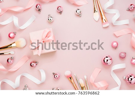 Frame with Christmas ball, gift, ribbon, cosmetic and decorations in pastel pink colour. Holiday Background. Beauty concept. Flat lay, top view