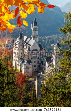 Neuschwanstein Castle under Sunlight with Mountain Hills on Background and colorful leafes, Amazing autumn Landscape. Picture of the fairy tale Castle near Munich in Bavaria, Germany. Postcard