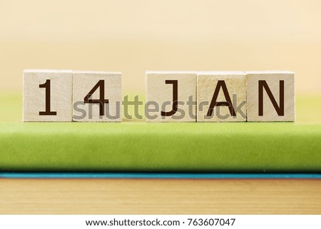Wooden cube shape calendar for JAN 14 on green book, table.  