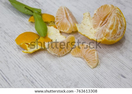 One mandarin peeled with its quarters, skin and green leaves on a white background striped with grey.