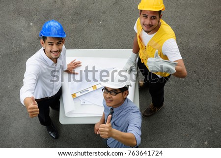 Top view of Asian happy Engineer team thumbs up after looking at construction paper blueprint to confirm project will complete on time. Successful Engineering men group of Heavy industry concept.