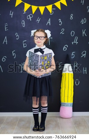 Young girl standing in front of chalkboard with letters of the alphabet and holding stick of chalk in hand